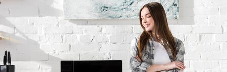 panoramic shot of smiling and attractive woman standing near microwave in kitchenの写真素材