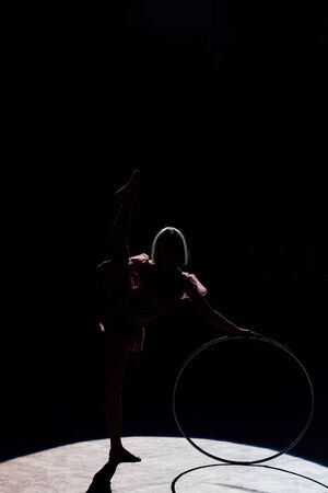 silhouette of flexible acrobat standing with hula hoop in arena of circusの写真素材