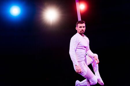 back light near handsome acrobat looking at camera while performing on black