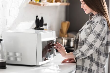 cropped view of smiling woman in shirt using microwave in kitchenの写真素材