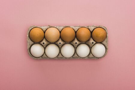 top view of chicken eggs in cardboard box on pink background