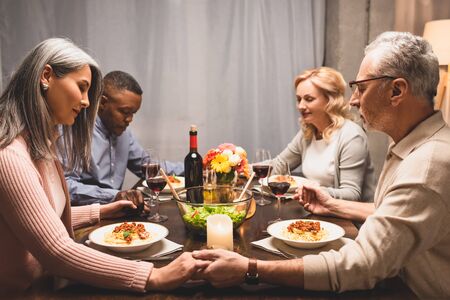 multicultural friends holding hands and praying during dinnerの写真素材