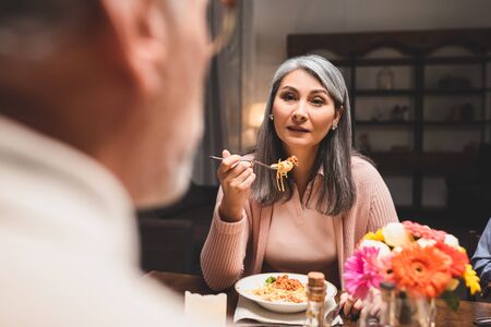 selective focus of asain woman eating pasta and looking at friend during dinnerの写真素材