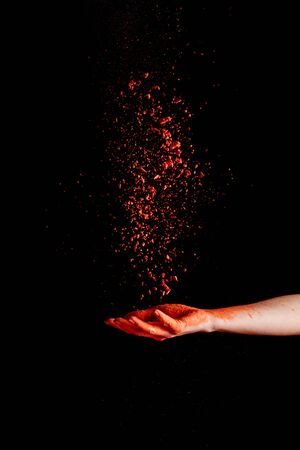 female hand with red colorful holi paint powder on black backgroundの写真素材
