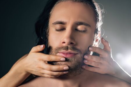 girl touching face of handsome man with closed eyes on grey with back lightの写真素材