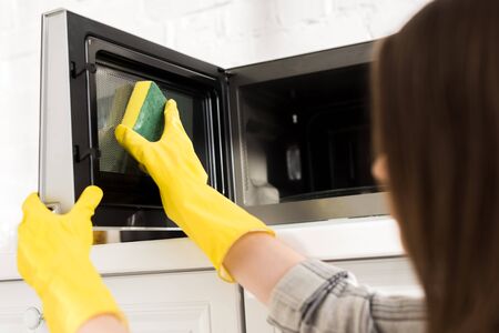 cropped view of woman in rubber gloves cleaning microwave with spongeの写真素材
