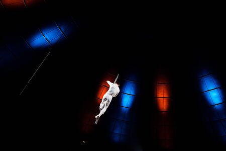 back view of acrobat performing on pole in arena of circusの写真素材