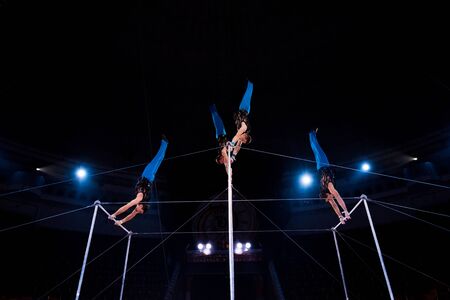 low angle view gymnasts performing on horizontal bars in arena of circus