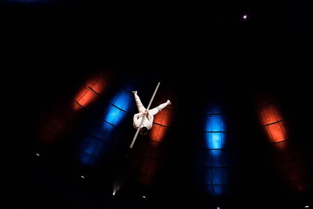 back view of acrobat balancing on metallic pole in arena of circus