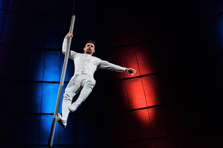 strong acrobat holding metallic pole while performing in circus