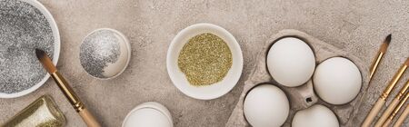 top view of chicken eggs, silver and golden glitter with paintbrushes on grey concrete surface, panoramic shotの写真素材