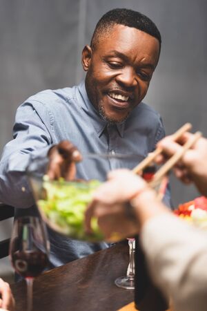 cropped view of woman giving owl with salad to african american friend during dinnerの写真素材
