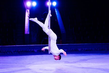 acrobat performing upside down on pole in arena of circus