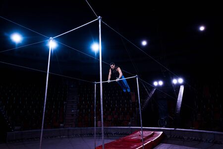 handsome gymnast performing on horizontal bars in circus