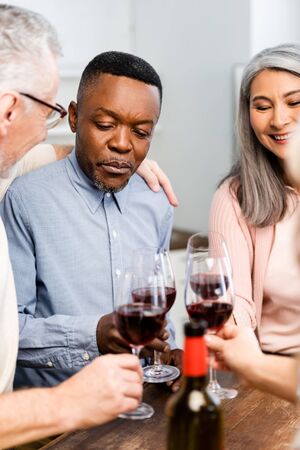 cropped view of smiling multicultural friends clinking with wine glasses in kitchenの写真素材
