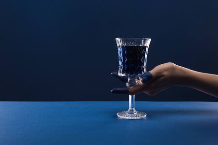 cropped view of female hand with painted fingers holding faceted glass with drink isolated on blue