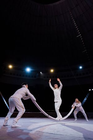 acrobats supporting man with outstretched hands ready to jump on pole in circusの写真素材