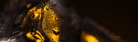 close up view of wet square ice cube with yellow illumination, panoramic shot