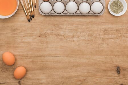 top view of orange watercolor paint and golden glitter in bowls near Easter eggs and paintbrushes on...
