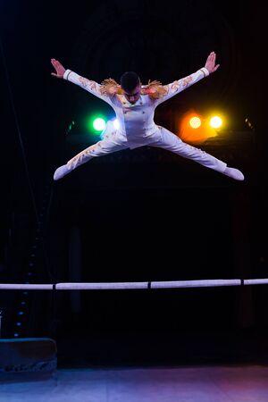 handsome gymnast in costume jumping near pole in arena of circus