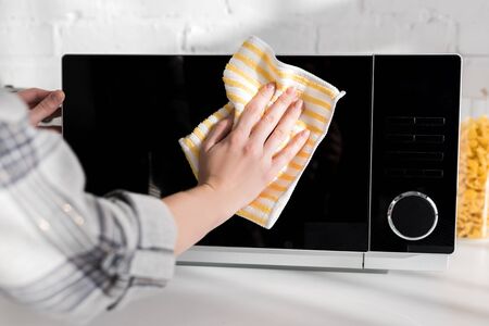 cropped view of woman cleaning microwave with rag in kitchenの写真素材