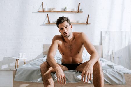 shirtless man looking at camera while sitting on bedの写真素材