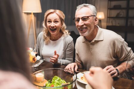 selective focus of smiling man and woman talking with friend during dinnerの写真素材