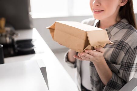 cropped view of smiling woman holding paper bag with popcorn near microwave in kitchenの写真素材