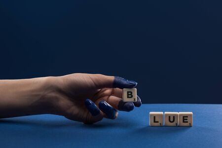 cropped view of female hand with painted fingers near cubes with blue lettering isolated on blueの写真素材