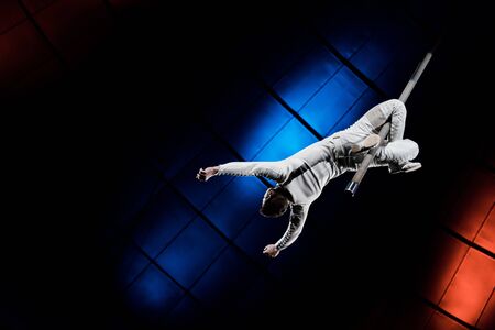 back view of strong acrobat balancing on metallic pole near blue and red lighting in circusの写真素材