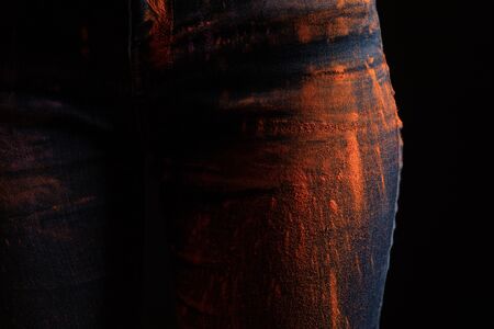 cropped view of woman with orange colorful holi paint powder on jeans isolated on black