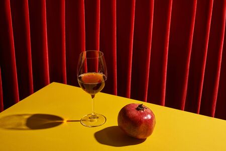 classic still life with pomegranate near glass of red wine on yellow table near red curtainの写真素材