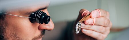 Panoramic shot of watchmaker in eyeglass loupe holding watch detail in tweezersの写真素材