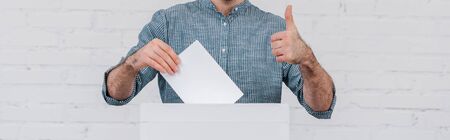 panoramic shot of voter showing thumb up while holding blank ballot
