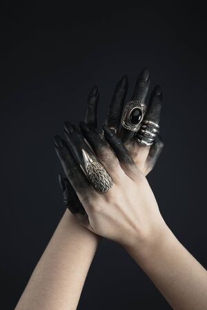 Cropped view of black painted hands of witch with jewelry rings isolated on blackの写真素材