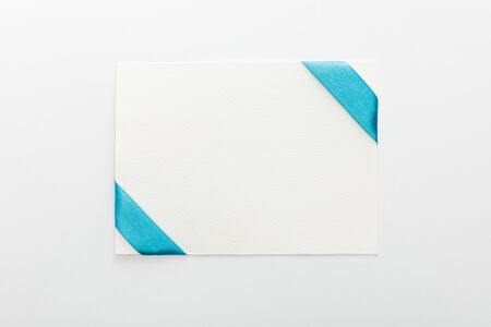 top view of blank card with blue decorative satin ribbon on white backgroundの写真素材