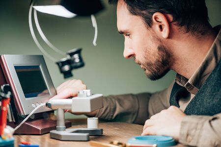 Side view of watchmaker using timegrapher while working at table