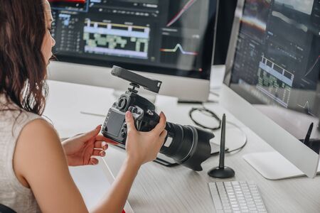 art editor holding digital camera near table with computer monitors