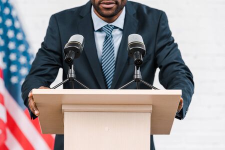 cropped view of african american speaker talking near microphones and american flag