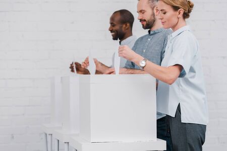 selective focus of happy multicultural citizens voting while standing near boxes
