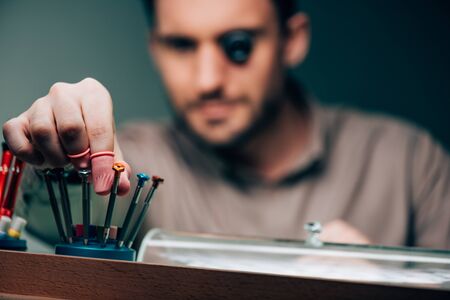 Selective focus of watchmaker in eyeglass loupe taking screwdriver