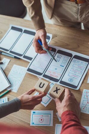 Cropped view of designers holding cubes with ux letters while working with layouts at table