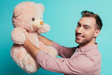 bearded smiling man holding teddy bear, isolated on blueの写真素材