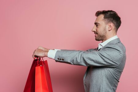 happy man holding shopping bags, isolated on pink