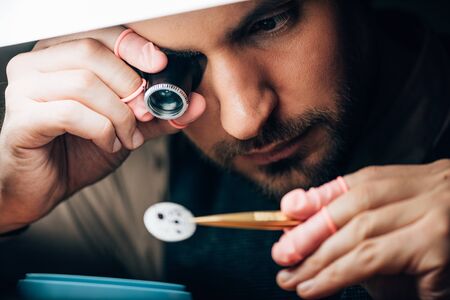 Selective focus of watchmaker holding eyeglass loupe and watch part by lampの写真素材
