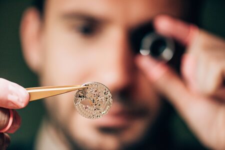 Selective focus of clockmaker holding watch part in tweezers