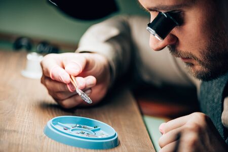 Side view of watchmaker holding watch part by tool tray on table