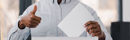 panoramic shot of african america voter holding blank ballot and showing thumb upの写真素材