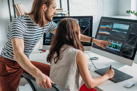 bearded art editor pointing with finger at computer monitor near womanの写真素材