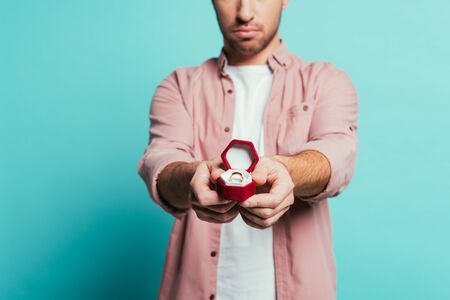 cropped view of serious man holding box with proposal ring, isolated on blue